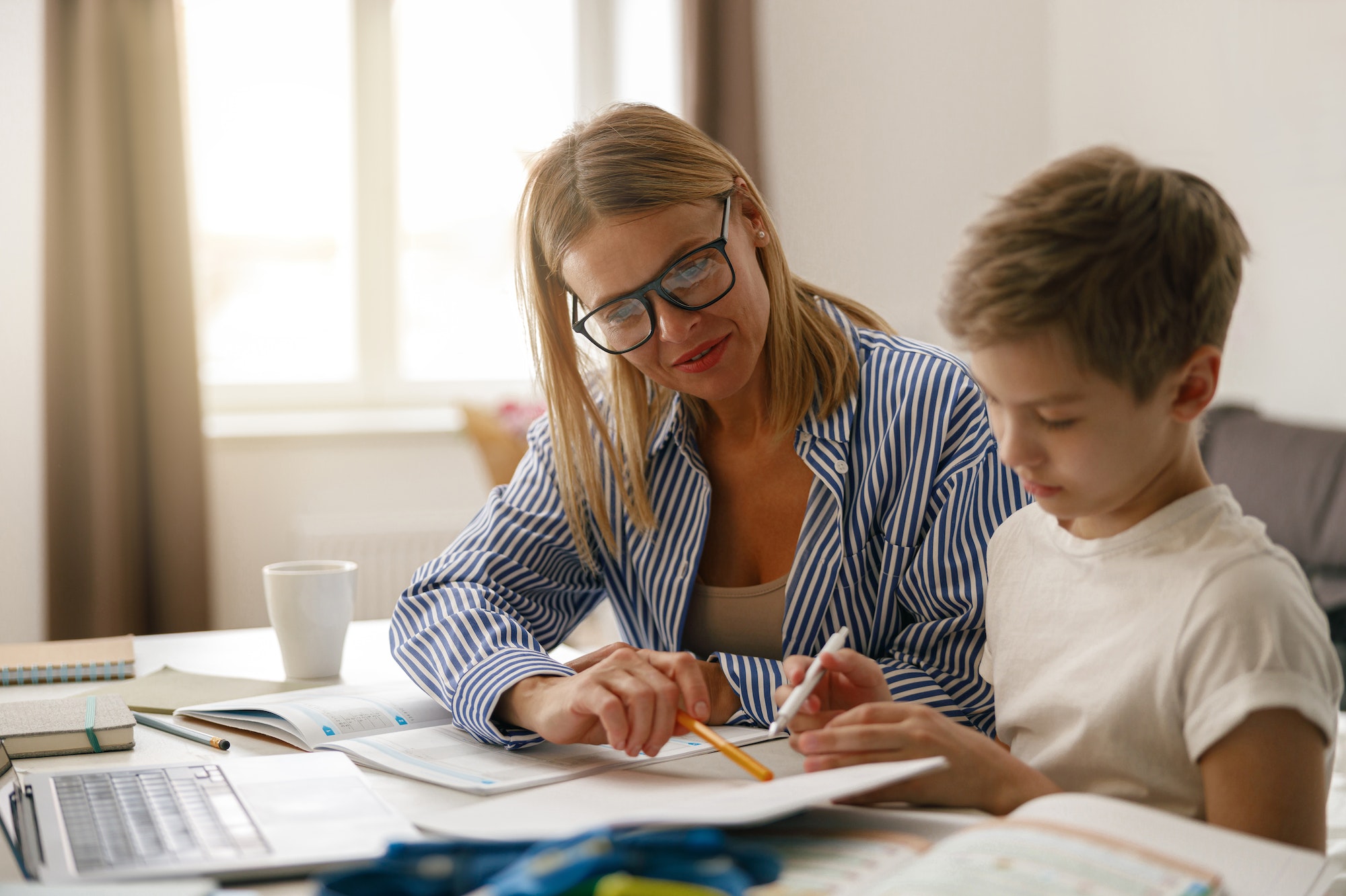 Happy mom and son doing homework and studying with laptop together. Home education